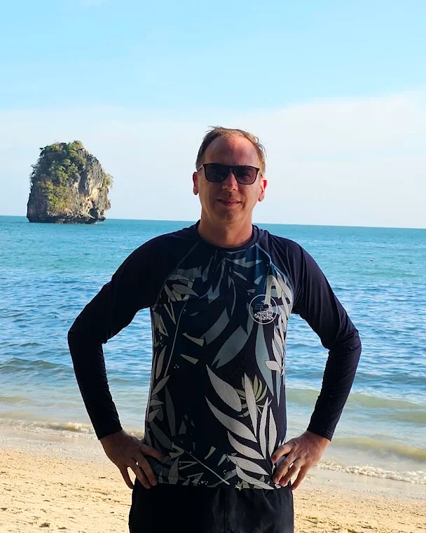 Man on a beach wearing a custom long-sleeve rashguard with a dark leaf print, made by Sportswear of Tomorrow