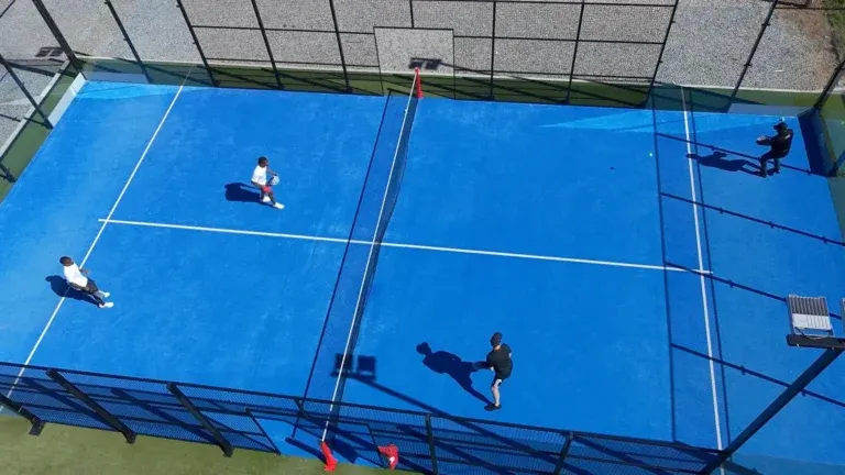 Aerial view of four players in a doubles match on a blue outdoor padel court, the setting padel brands design apparel for