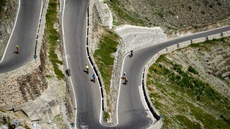 Road cyclists climbing the hairpin bends of a high Alpine pass, seen from above
